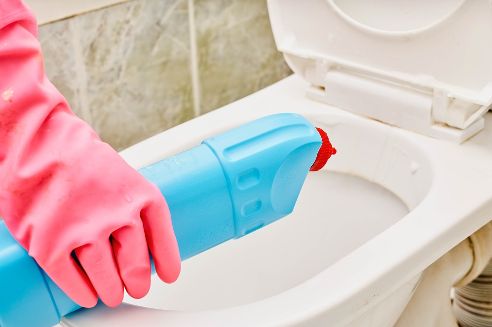 Žena v rukavicích nalévá WC čistič do mísy