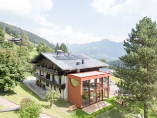 Moderní rodinná chata jako přístavek k tradiční alpské budově. Výrazný červený obklad zaujme na kilometry daleko